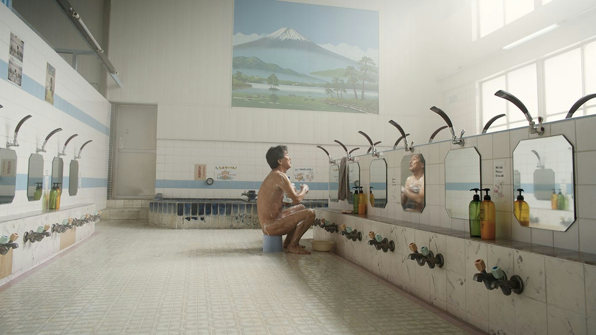 Ein Mann sitzt nackt in einem Badehaus vor einem Spiegel.