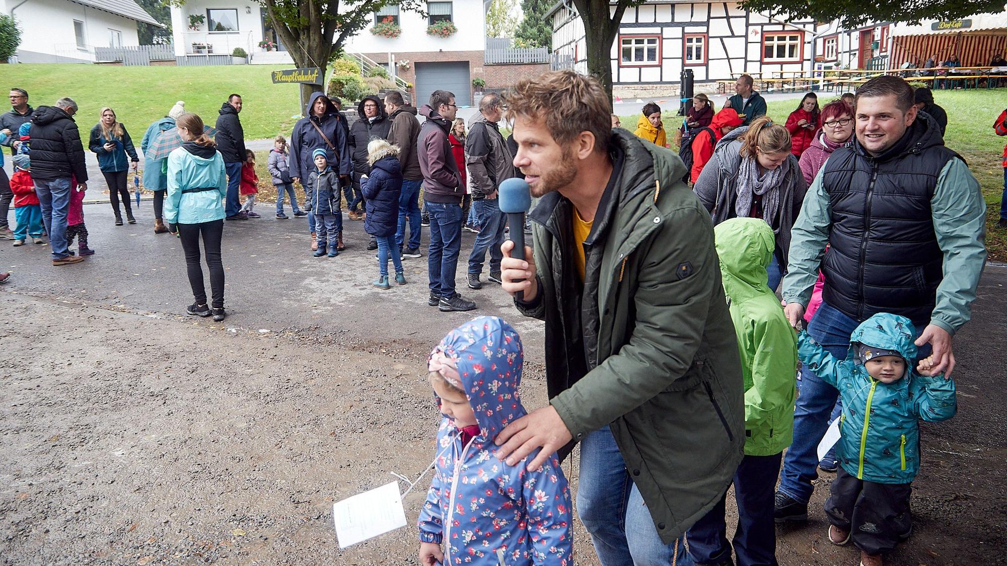 Der Kinderliedersänger Uwe Reetz hält ein Mikrofon in der Hand. Um ihn herum stehen einige Kinder mit ihren Eltern.