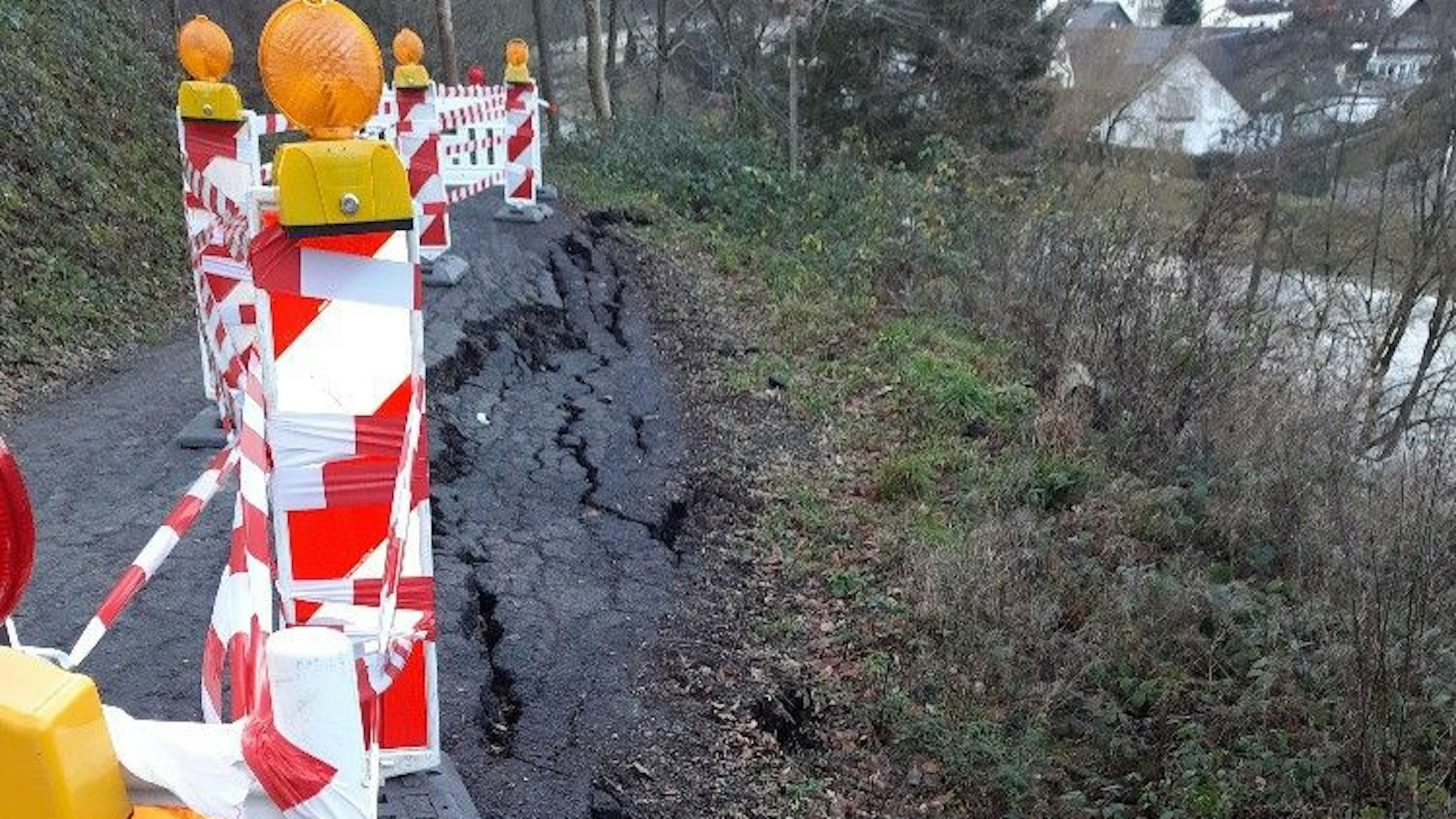 Die asphaltierte Abbruchkante am Hang ist mit rot-weißen Baken und Flatterband gesichert.