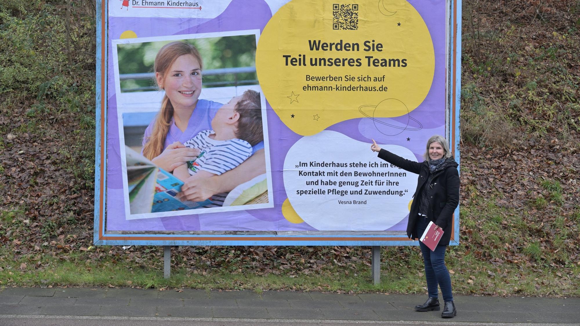 Frau steht vor einem großen Plakat und zeigt darauf