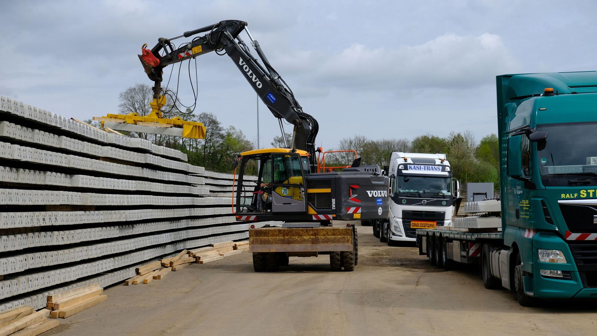 Auf dem ehemaligen Sägewerksgelände in Kall werden von einem Bagger mit Greifarm Bahnschwelllen aus Beton von einem Lkw abgeladen.