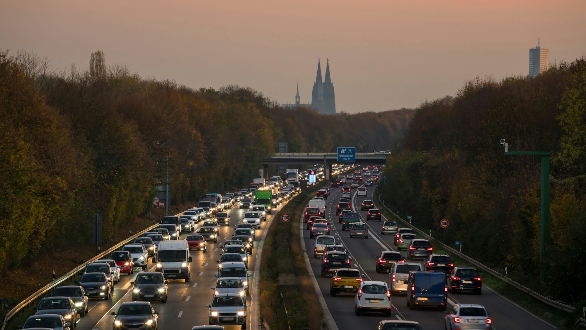 Stau auf der Autobahn Richtung Köln und aus Köln heraus bei rötlichem Himmel, im Hintergrund sieht man den Kölner Dom.