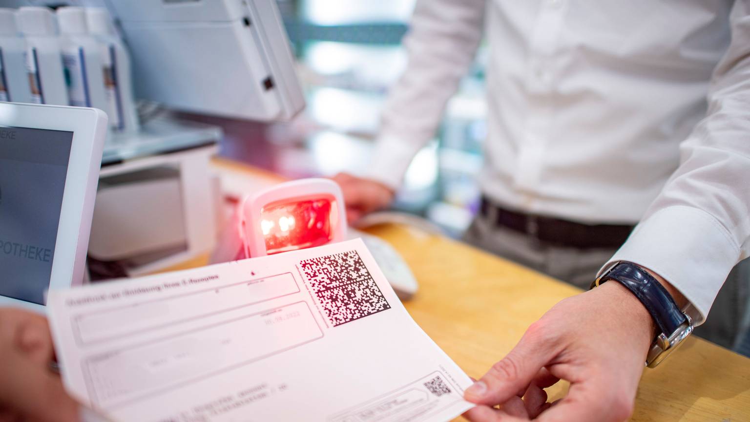 Ein Rezept mit einem QR-Code wird einem Mitarbeiter in einer Apotheke überreicht.