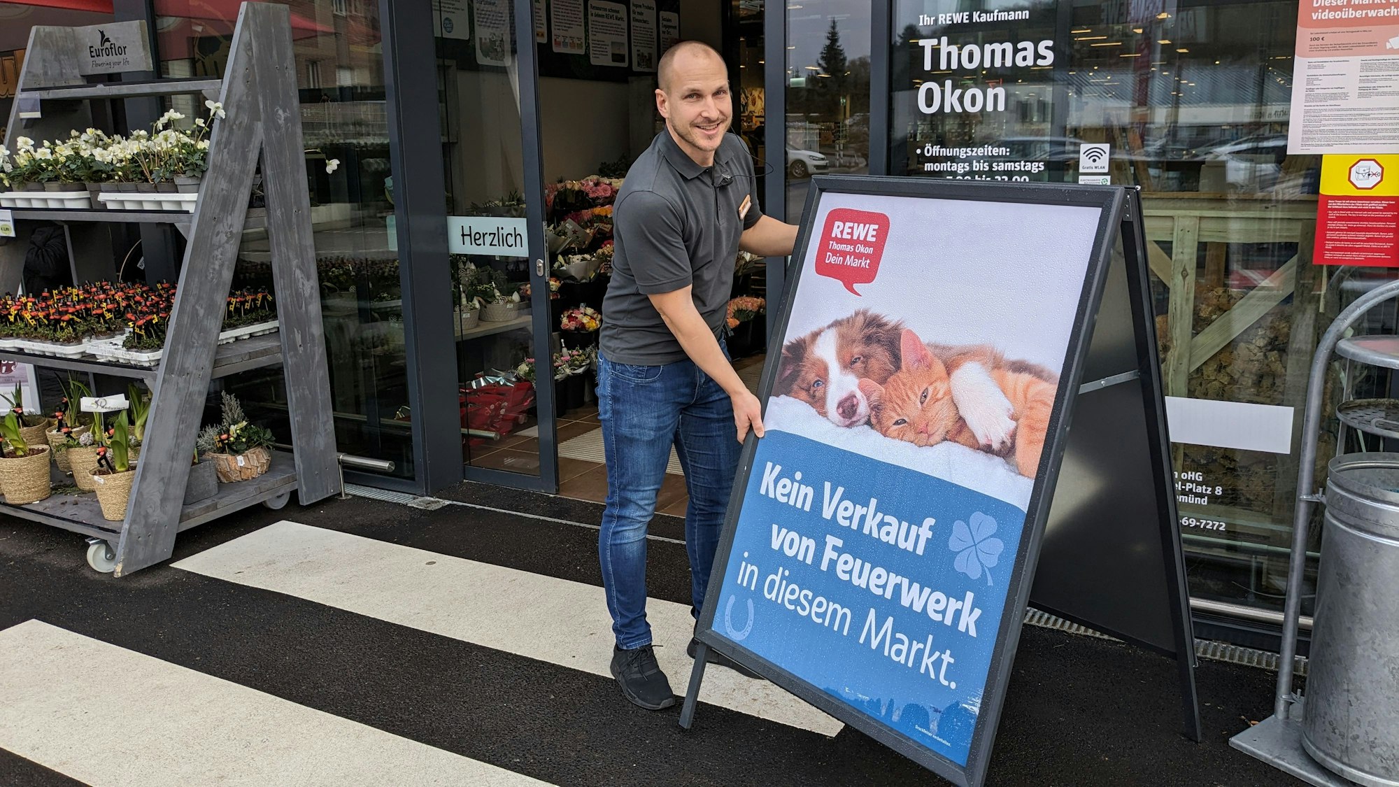 Thomas Okon stellt am Eingang seines Supermarkts ein Schild mit einem Hund und einer Katze auf, das darauf hinweist, dass dort keine Feuerwerkskörper verkauft werden.