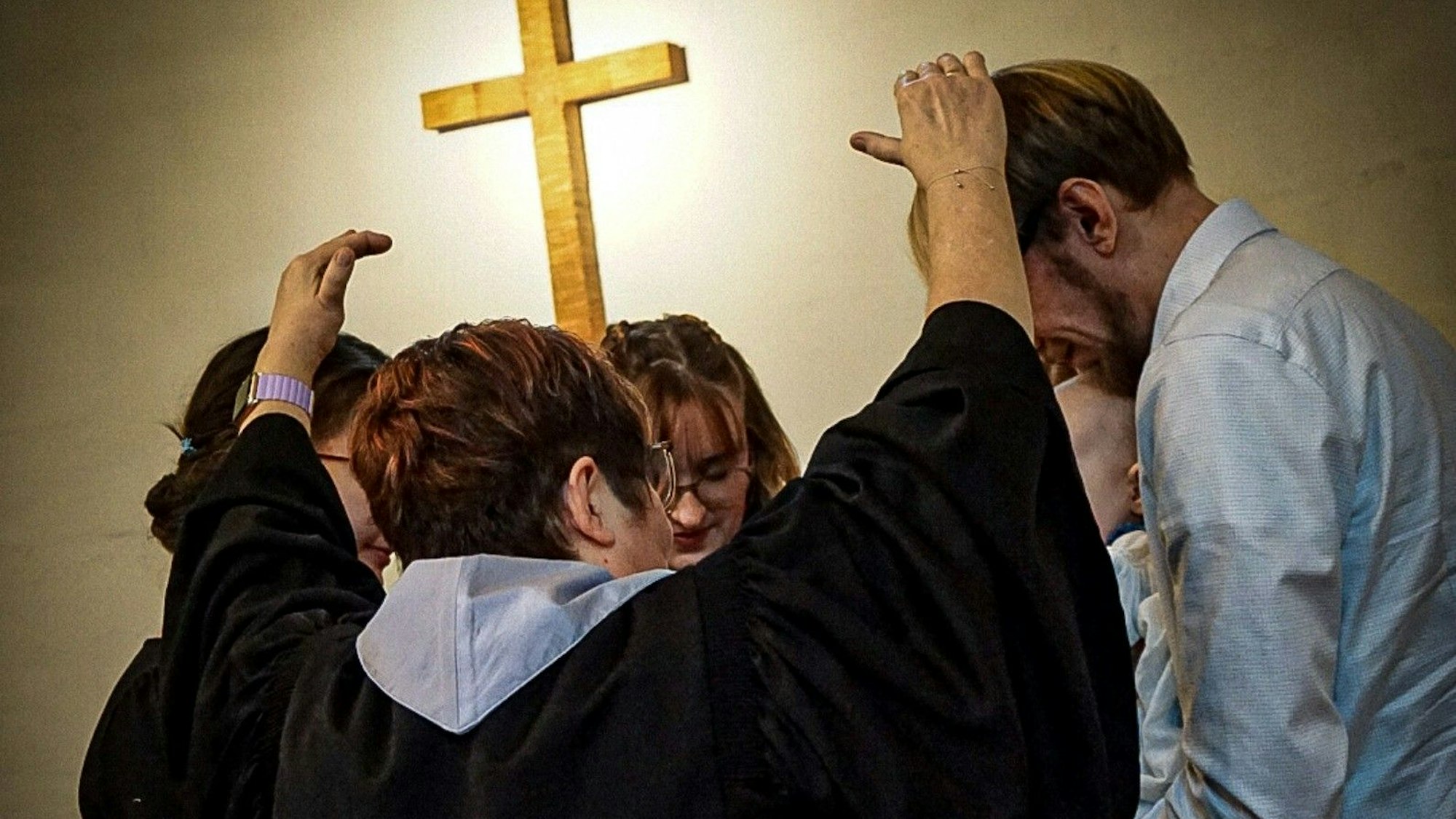 Prädikantin Sibylle Thon segnet ihr Enkelkind und ihre Familie. Im Hintergrund ist ein Kreuz zu sehen.