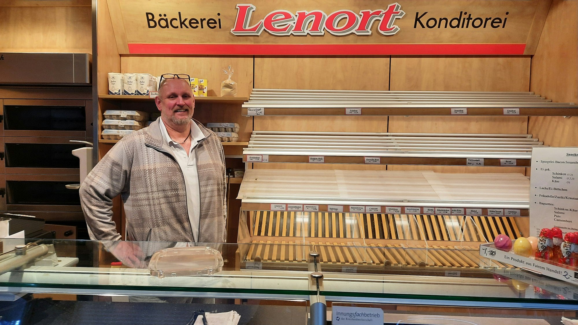 Blick auf einen Bäcker vor den leeren regalen einer Bäckerei.