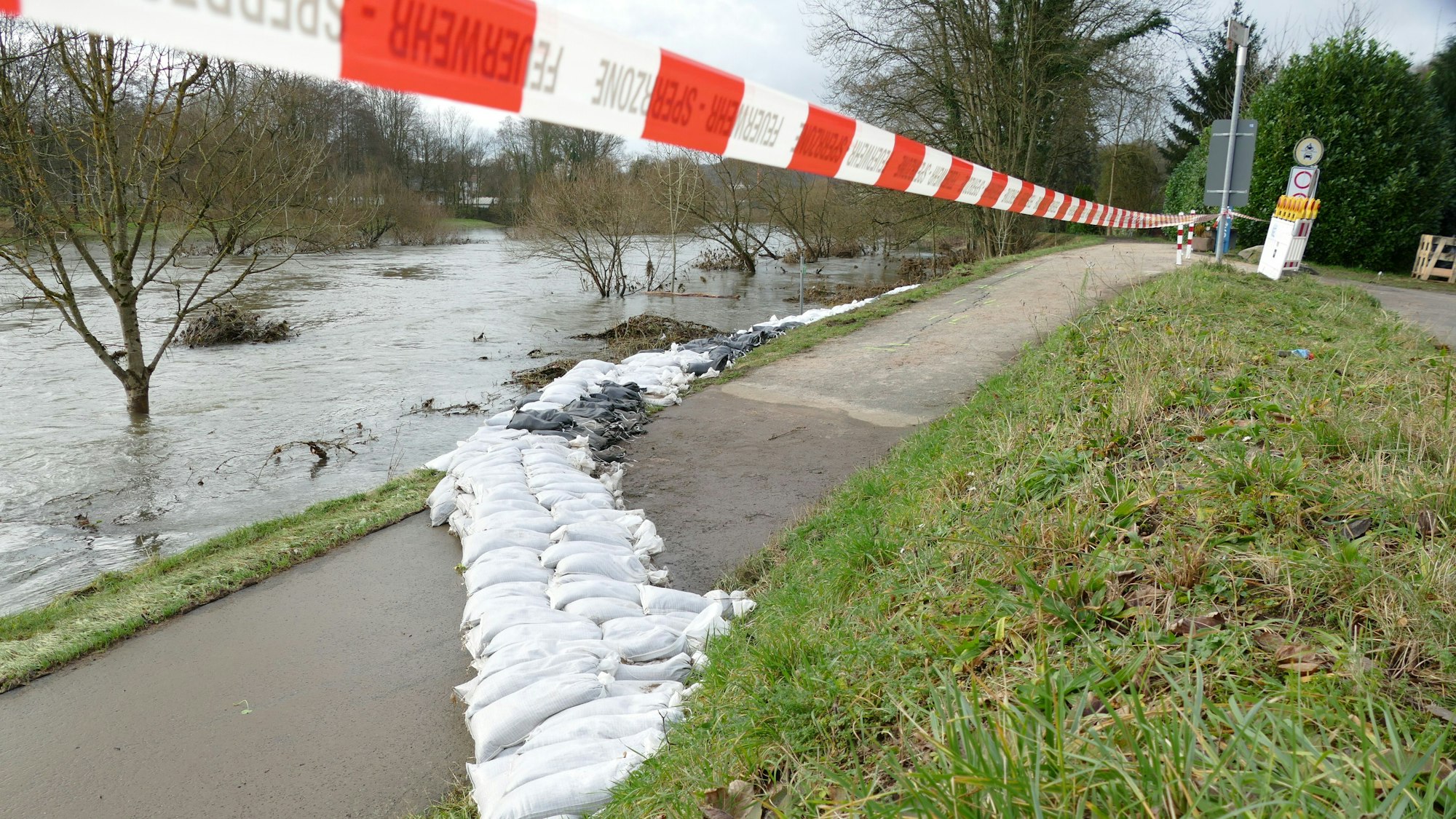 Sandsäcke liegen verteilt vor einem Gewässer.