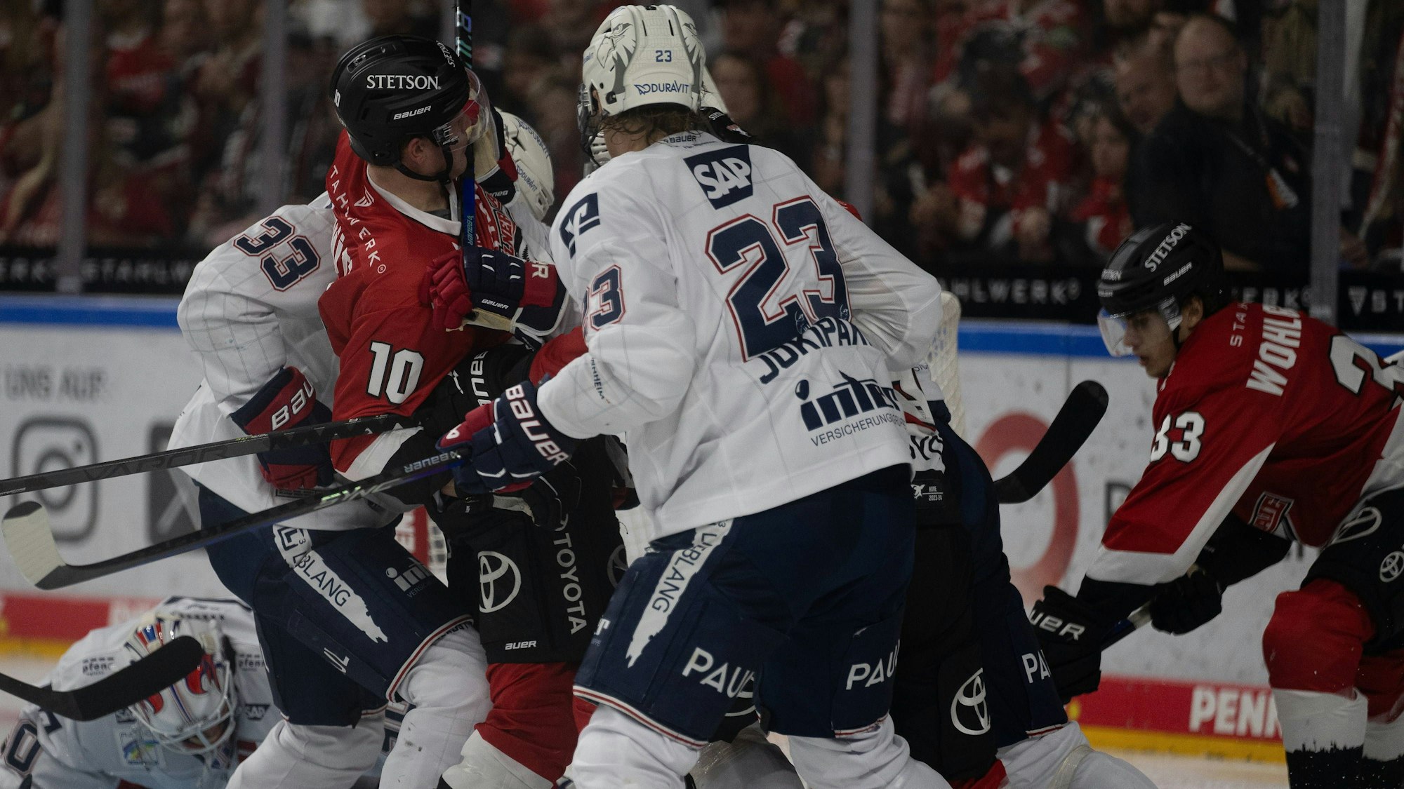 Mehrere Eishockeyspieler kämpfen dicht gedrängt um den Puck.