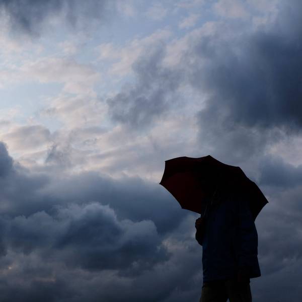 Ein Mann geht mit einem Regenschirm vor aufziehenden dunklen Wolken spazieren.