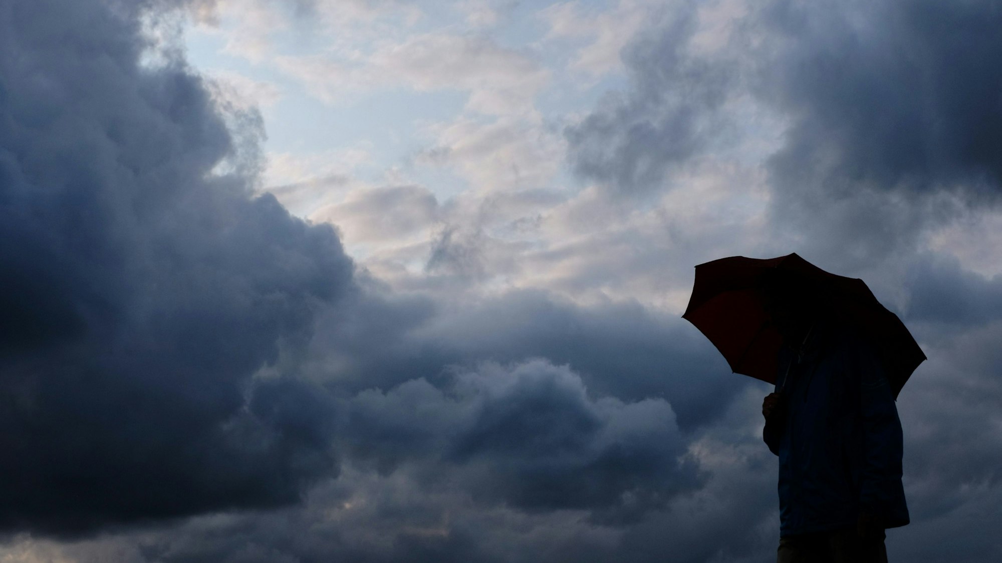 Ein Mann geht mit einem Regenschirm vor aufziehenden dunklen Wolken spazieren.