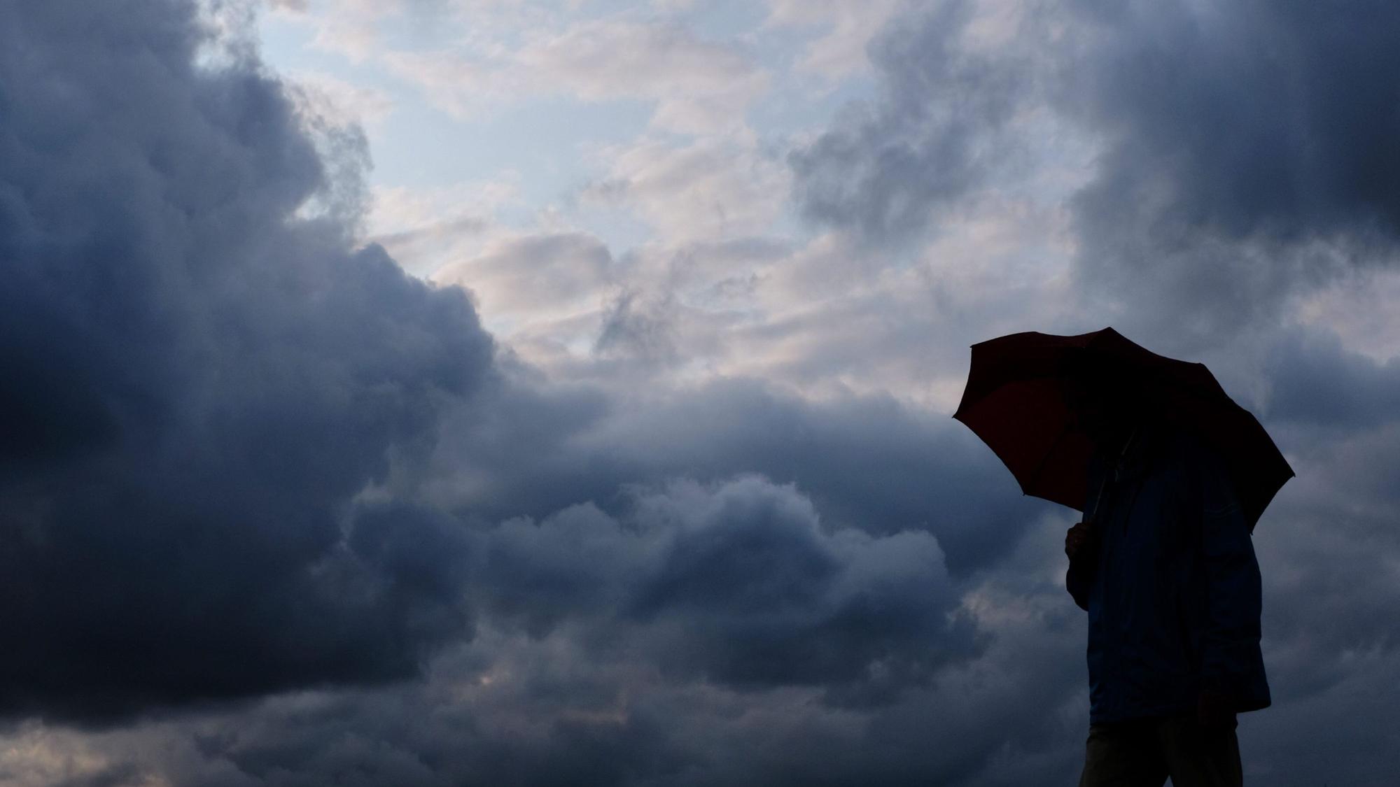 Eine Person geht mit einem Regenschirm vor aufziehenden dunklen Wolken spazieren. (Symbolbild)