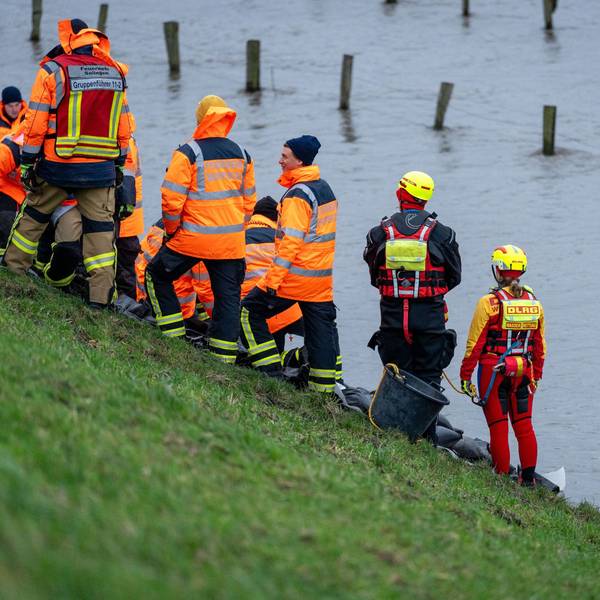 Mitglieder von Feuerwehr und DLRG stehen am Rand einer großen Wasserfläche.