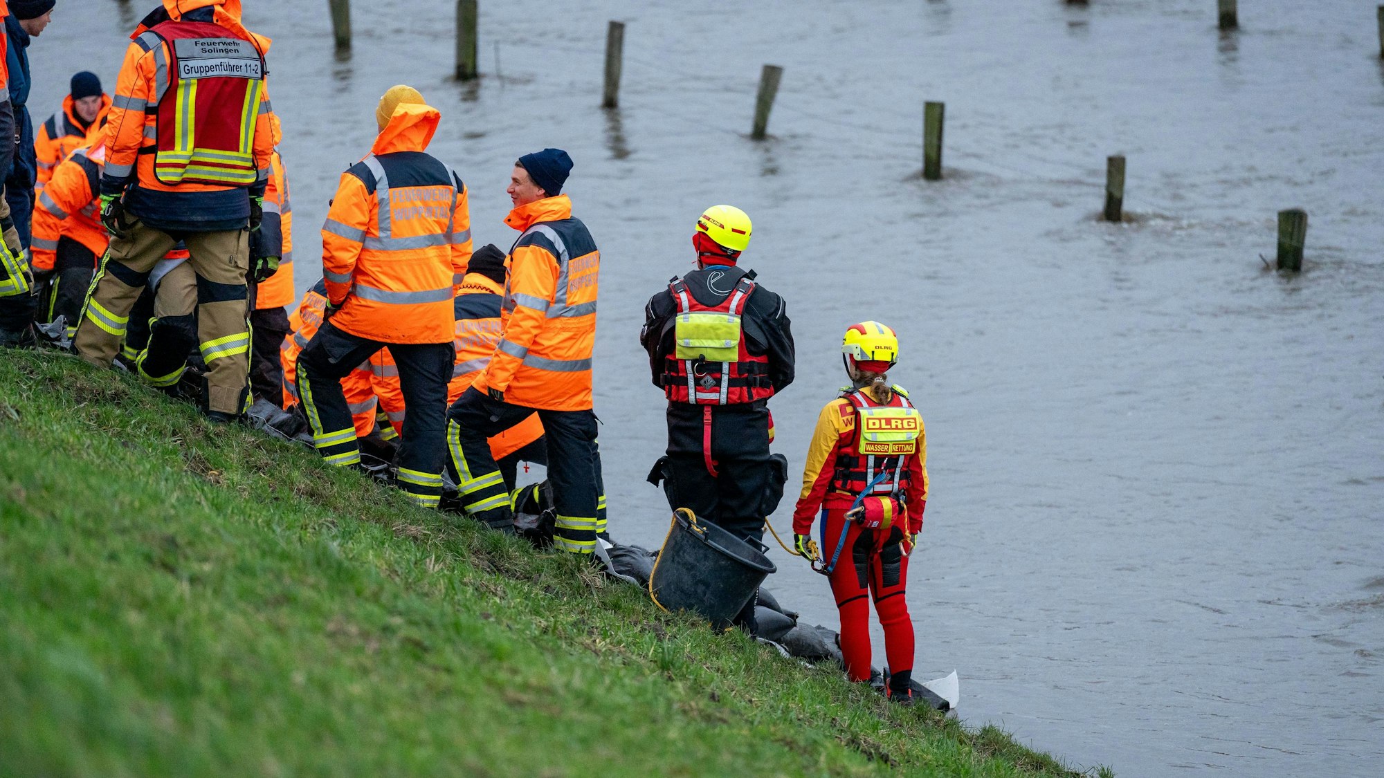 Mitglieder von Feuerwehr und DLRG stehen am Rand einer großen Wasserfläche.