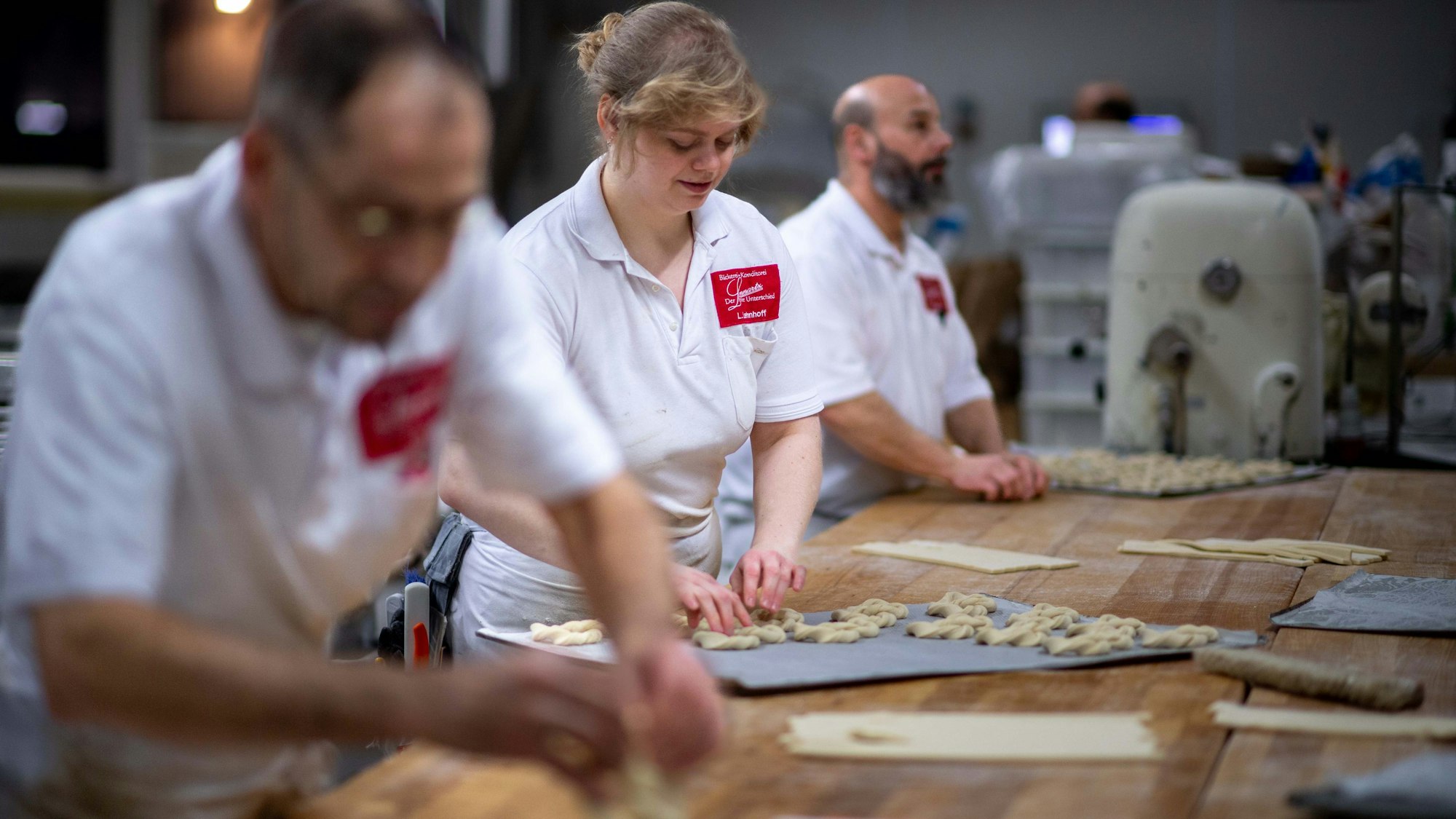Das Bild zwei drei Bäcker, die an einem langen Tisch das Neujahrsgebäck zubreiten.