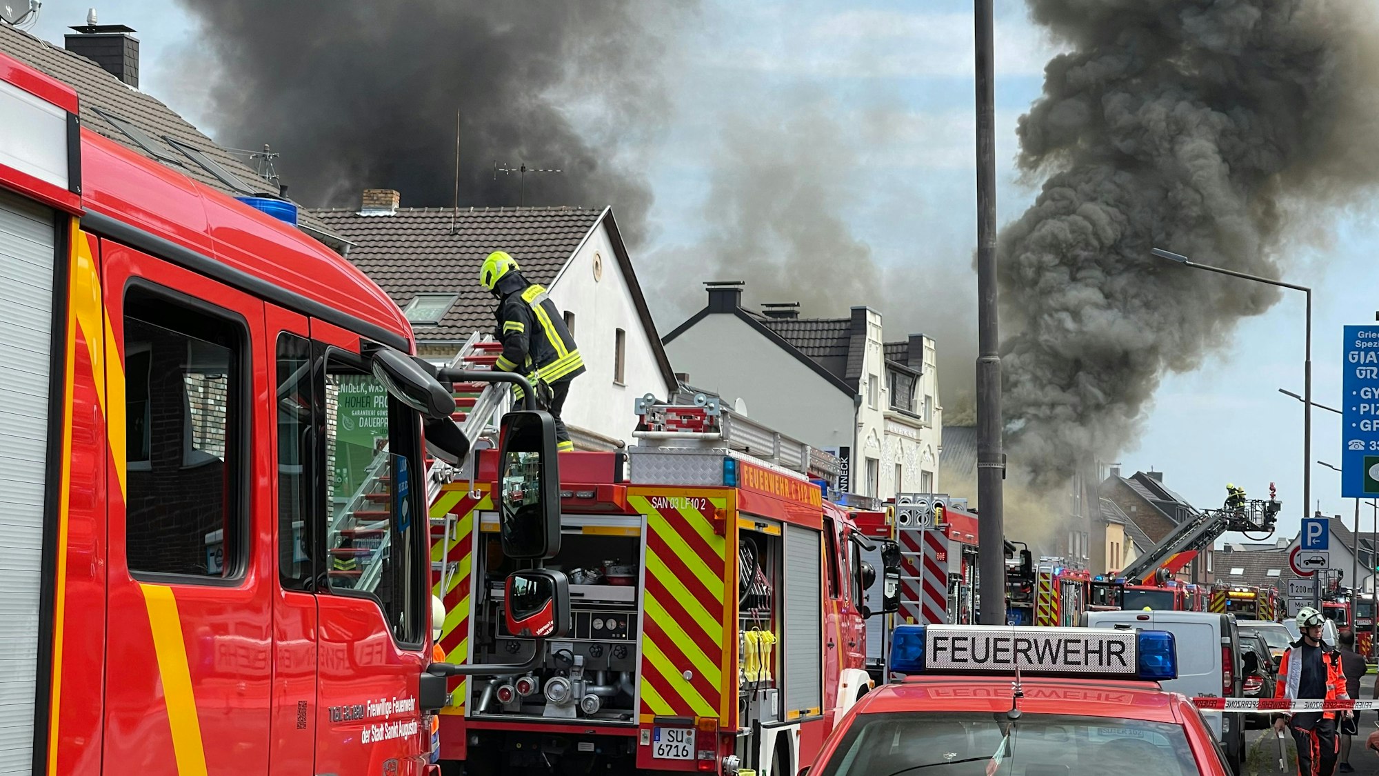 Viele Feuerwehrfahrzeuge stehen ij einer Straße, schwarzer Qualm dringt aus einem Gebäude.