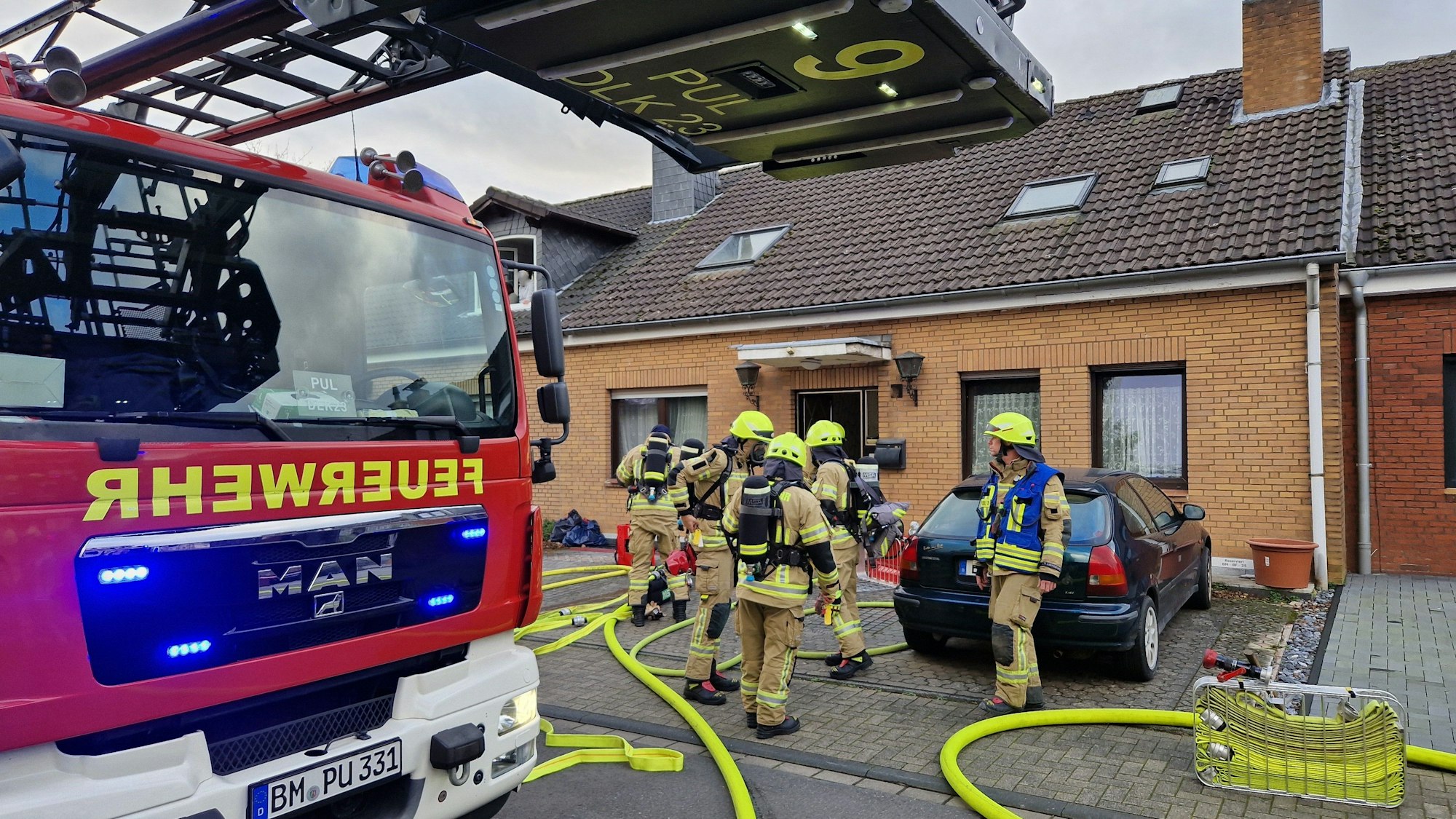 Es ist ein Haus zu sehen, vor dem mehrere Feuerwehrleute und ein Löschfahrzeug stehen.