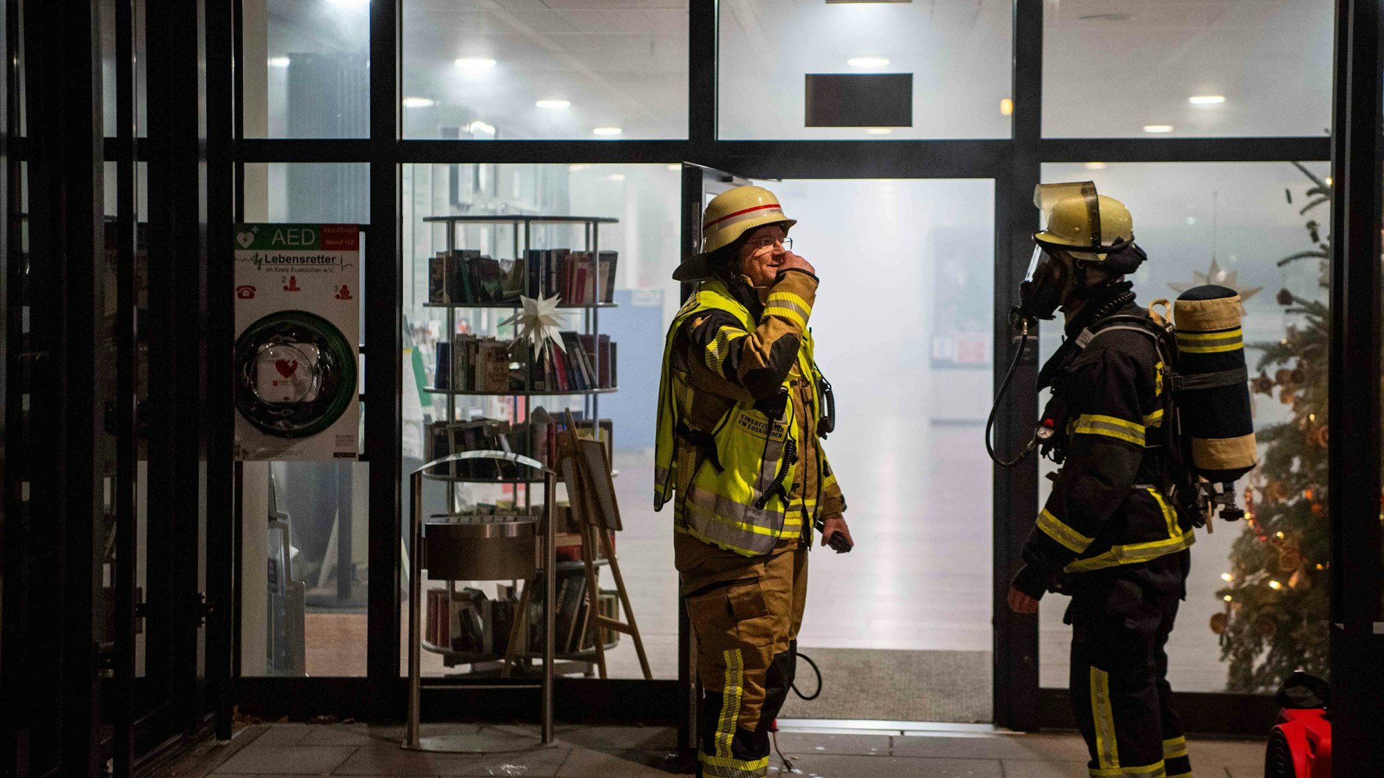 Zwei Feuerwehrleute, einer mit Atemschutzausrüstung, vor dem verrauchten Foyer der Kreisverwaltung in Euskirchen.