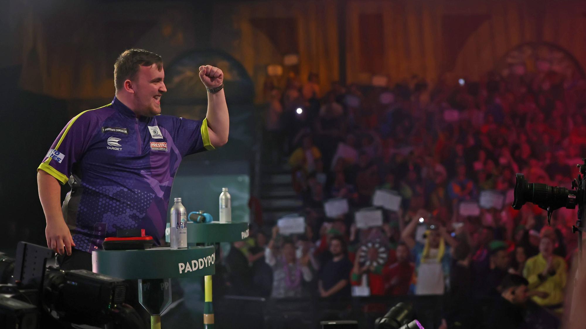 Der Jugendliche Dartspieler Luke Littler hebt triumphierend die Faust vor einer Menge.