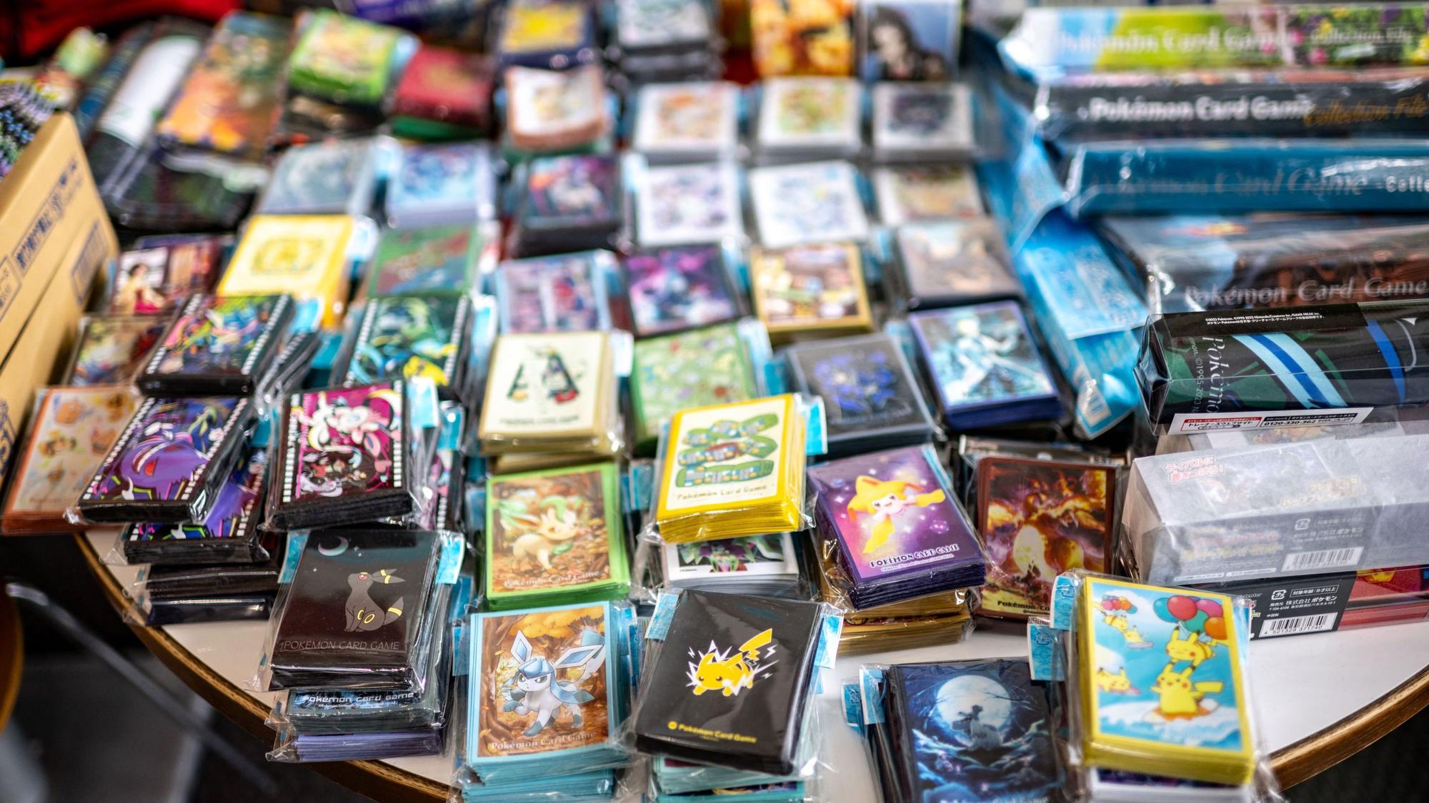Auf einem Tisch sind eine Vielzahl an Pokémon-Karten inklusive Hüllen und weiterem Zubehört aufgetürmt.
