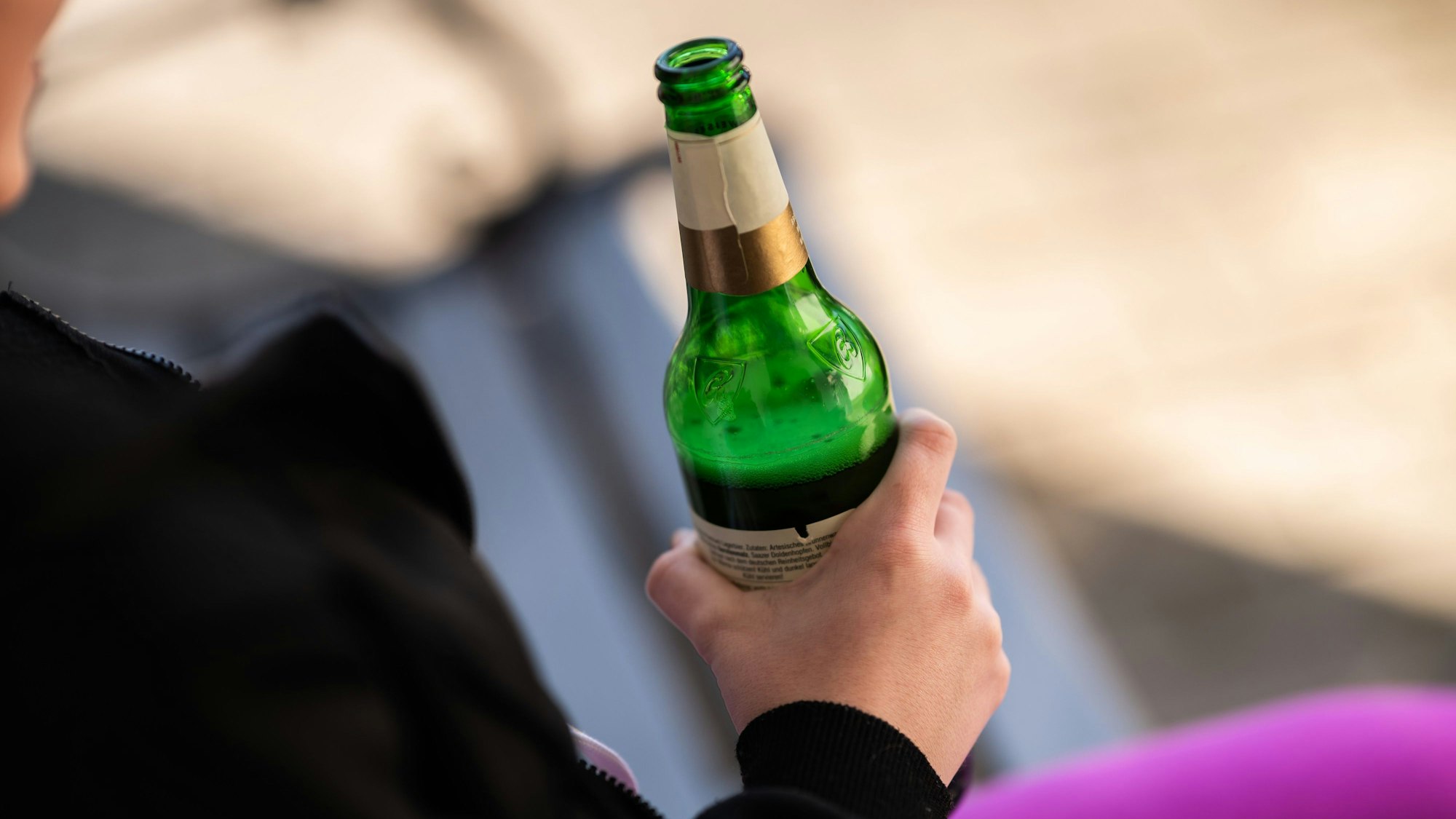 Eine Person hält vor ihrem Haus eine Flasche Bier in der Hand (Symbolbild).