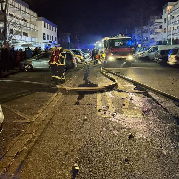 Auf dem Bild sind Feuerwehrleute und -autos in einem nächtlichen Einsatz zu sehen, im Hintergrund Blaulicht.