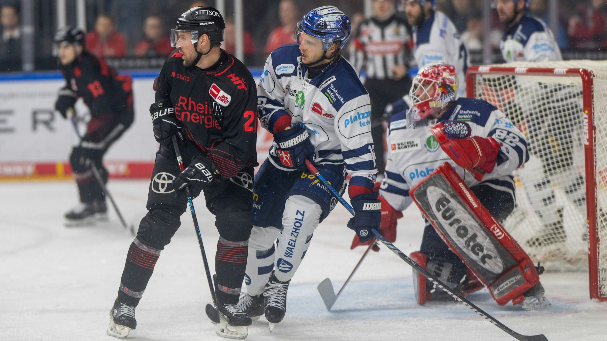 Zwei Eishockeyspieler stehen nah beieinander vor einem Tor mit einem weiteren Spieler.