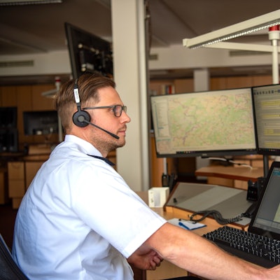 Nico Grocki, einer der Disponenten in der Rettungsleitstelle des Kreises Euskirchen, sitzt mit einem Headset auf dem Kopf an seinem Arbeitsplatz vor zahlreichen Monitoren.