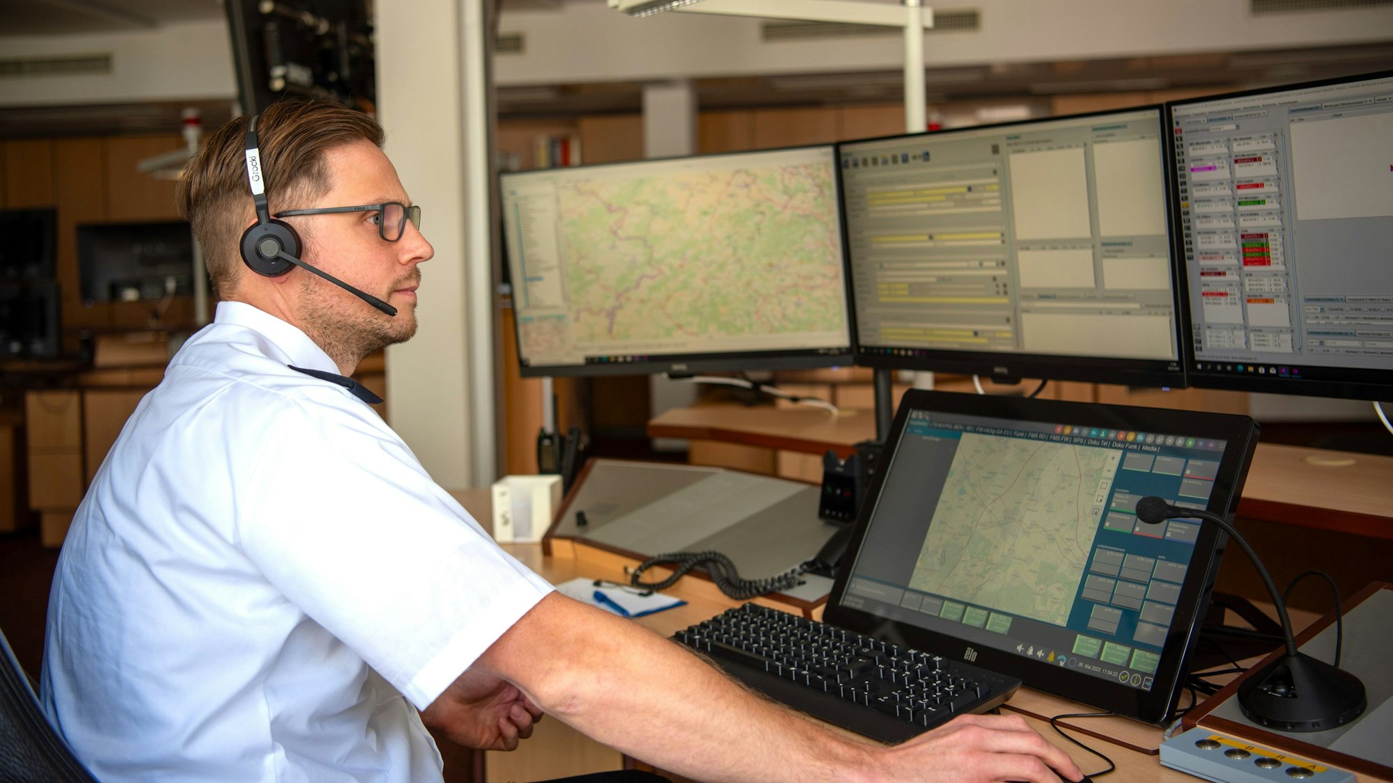 Nico Grocki, einer der Disponenten in der Rettungsleitstelle des Kreises Euskirchen, sitzt mit einem Headset auf dem Kopf an seinem Arbeitsplatz vor zahlreichen Monitoren.