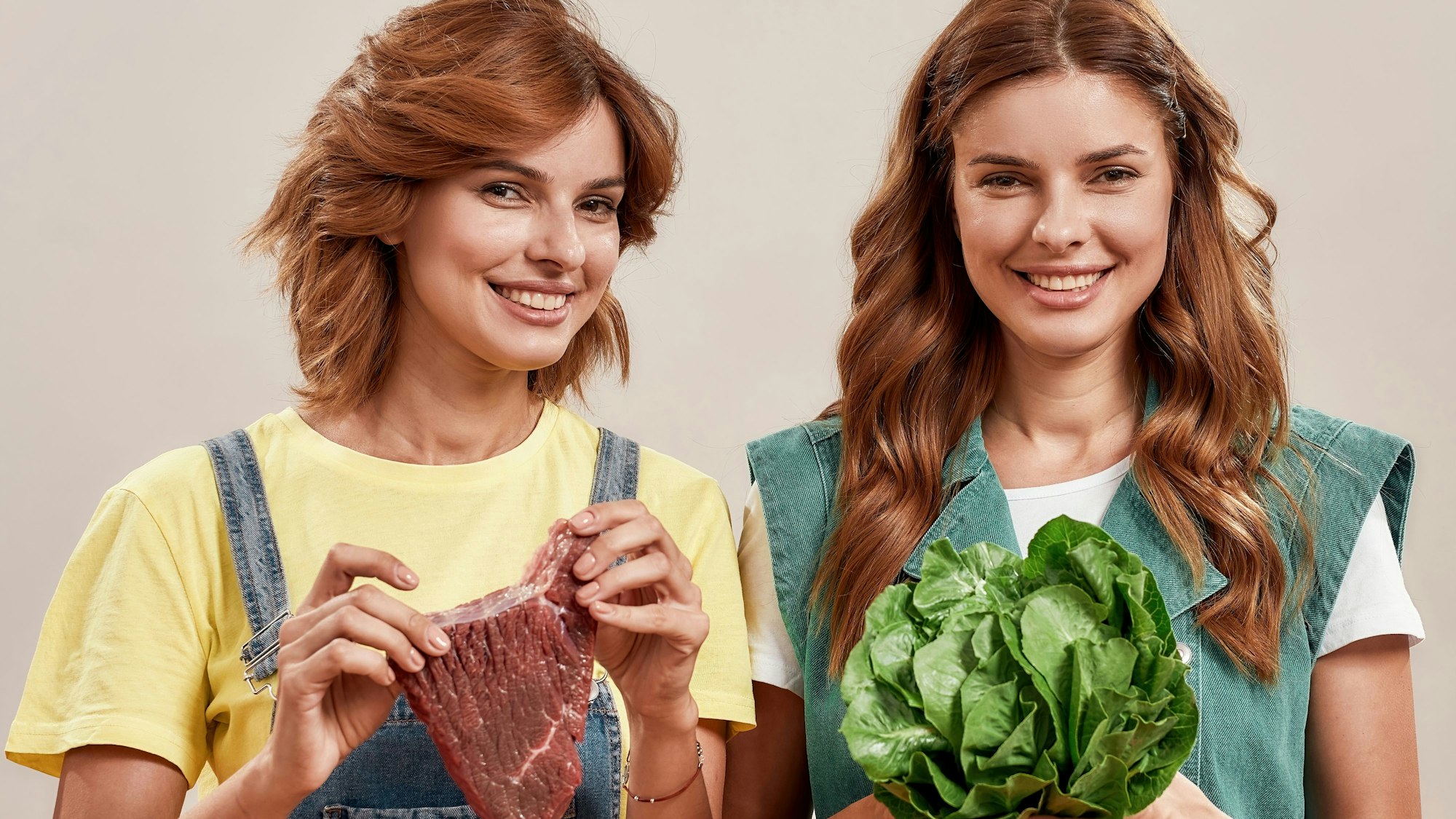 Zwillingsschwestern halten Essen in der Hand: Eine ein Stück Fleisch, die andere einen Kopfsalat. Symbolbild