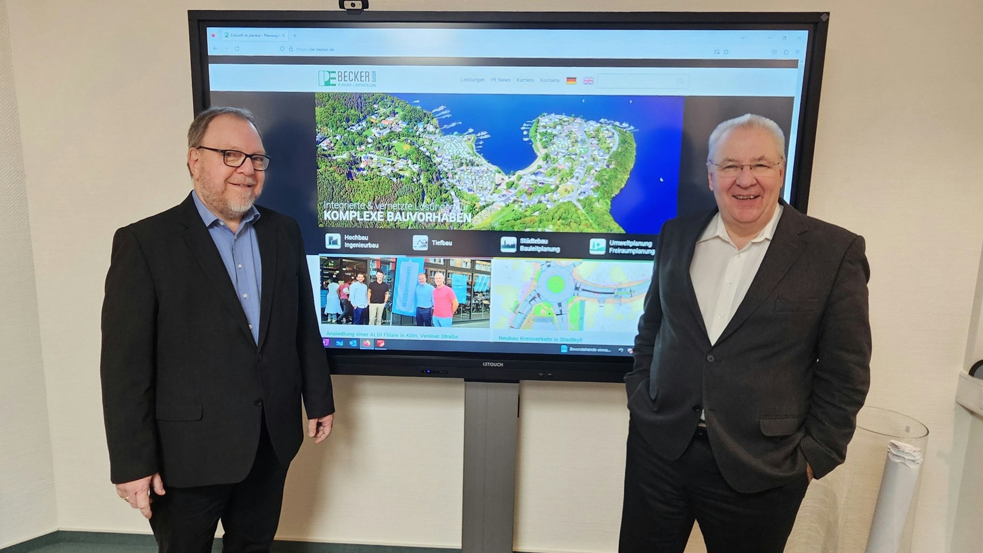 Geschäftsführer Andreas Göttgens und Bernd Becker stehen vor einem großen Monitor.