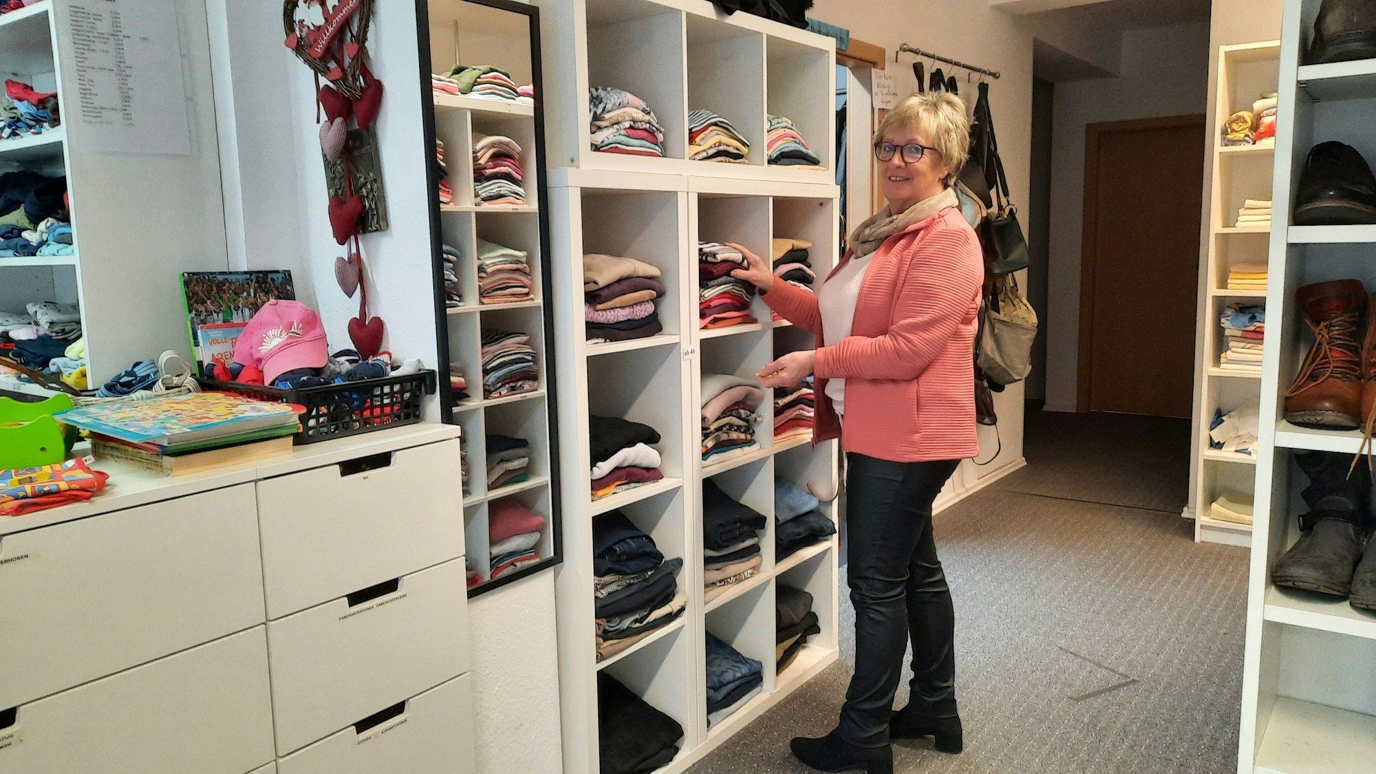 Uschi Sauermann vom Vorstand des Trägervereins der Kleiderkammer Frielingsdorf sortiert Anziehsachen in einem Regal.