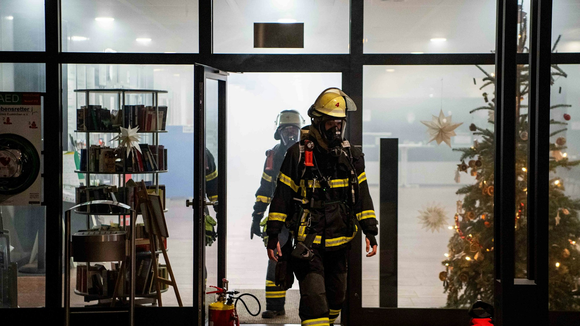 Zwei Feuerwehrleute mit Atemschutzgeräten kommen aus dem Kreishaus. Innen ist alles voller Rauch.
