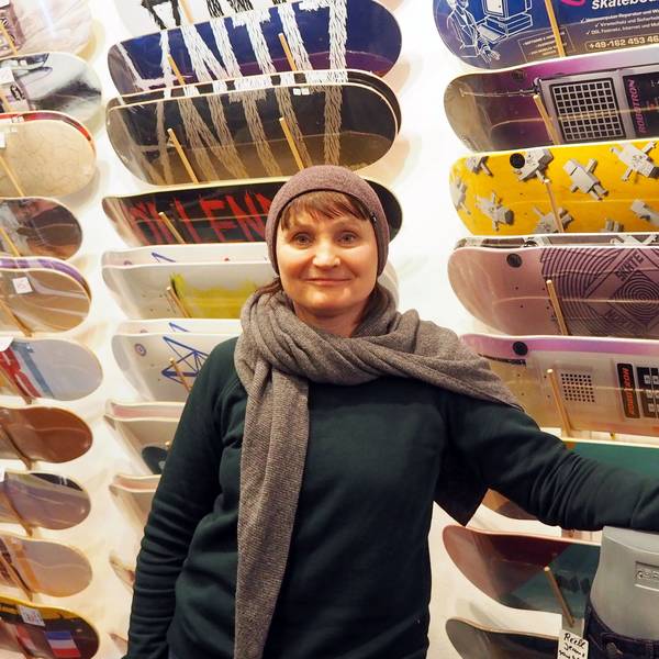 Eine Frau in Pulli, Schal und Mütze steht vor einer Wand, an der Skateboards in vielen Designs hängen.