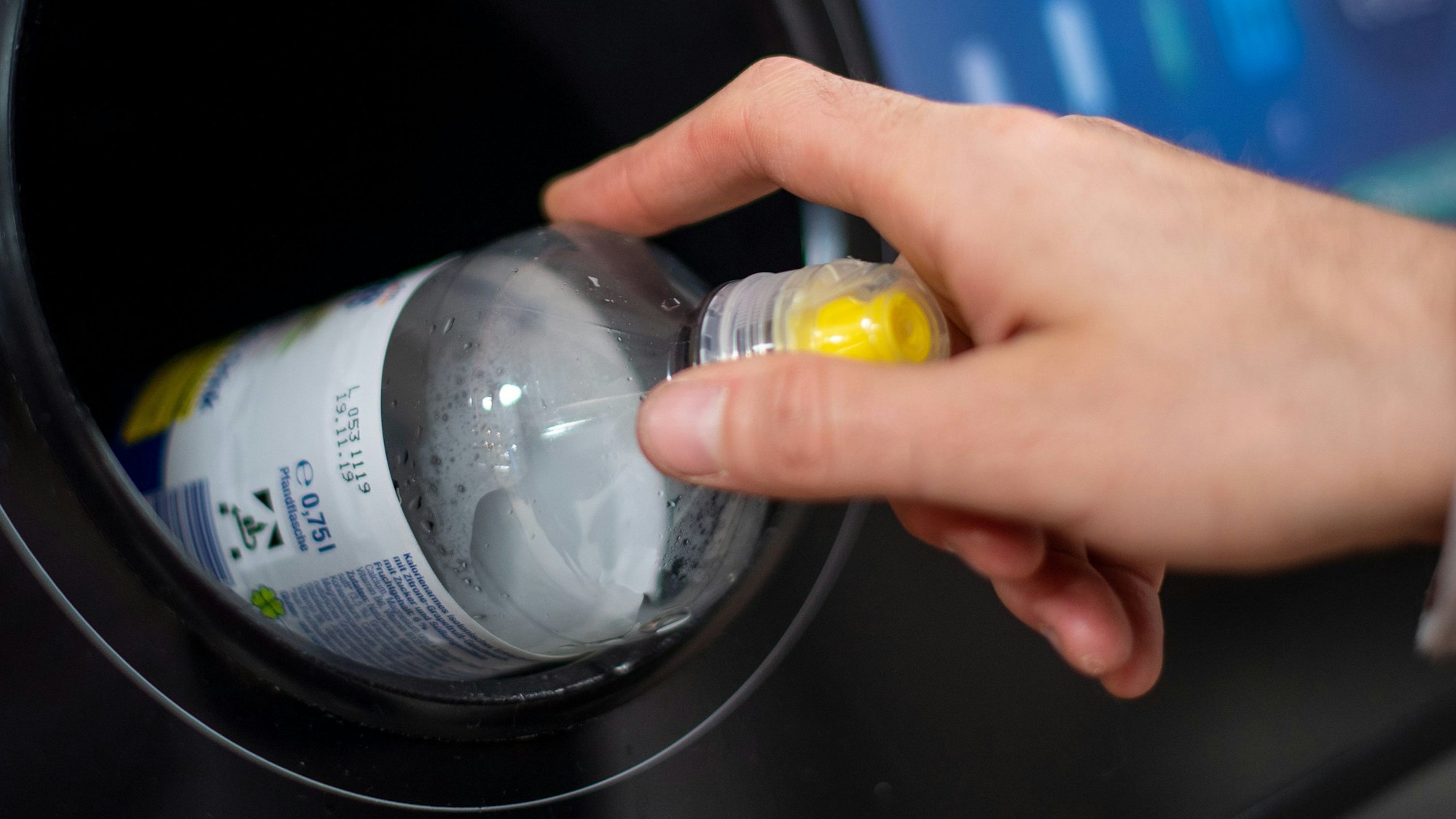 Eine Hand wirft eine Mehrwegflasche in einen Pfandflaschenbehälter.