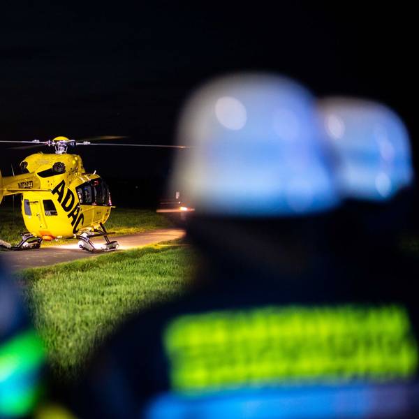 Das Bild zeigt einen Rettungshubschrauber, der auf einem Wirtschaftsweg in der Nacht gelandet ist. Drei Feuerwehrleute sind im Vordergrund zu sehen.