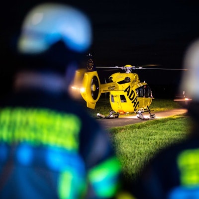 Das Bild zeigt einen Rettungshubschrauber, der auf einem Wirtschaftsweg in der Nacht gelandet ist. Drei Feuerwehrleute sind im Vordergrund zu sehen.
