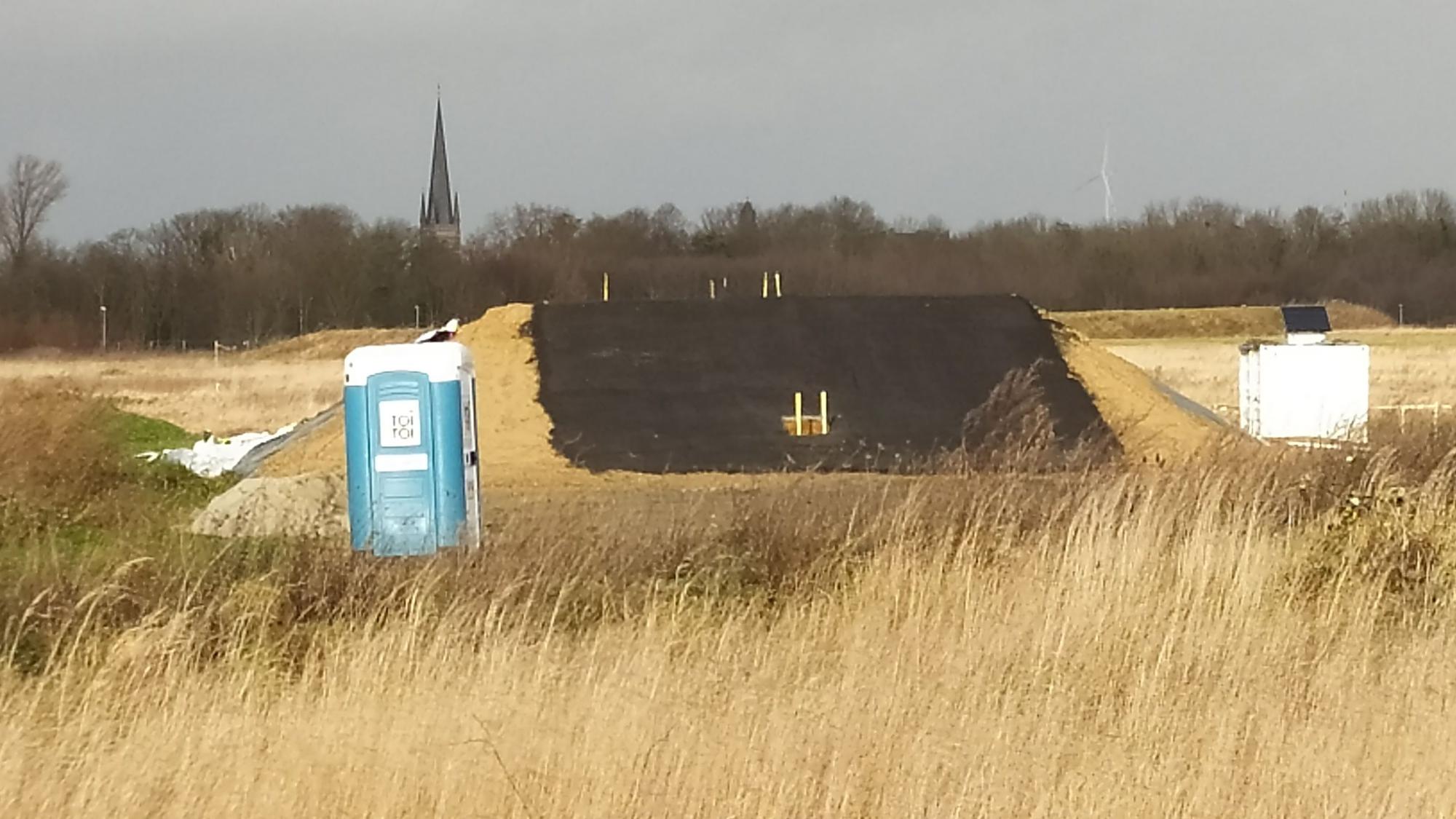 Eine künstlicher Hügel, ein Toilettenhäuschen und ein kleiner weißer Baucontainer markieren die Stelle, an der gebaut worden ist.