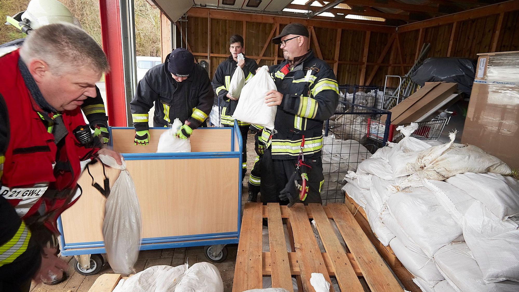 Mehrere Feuerwehrleute aus Gemünd stehen in einer Lagerhalle. Dort holen sie Sandsäcke ab.
