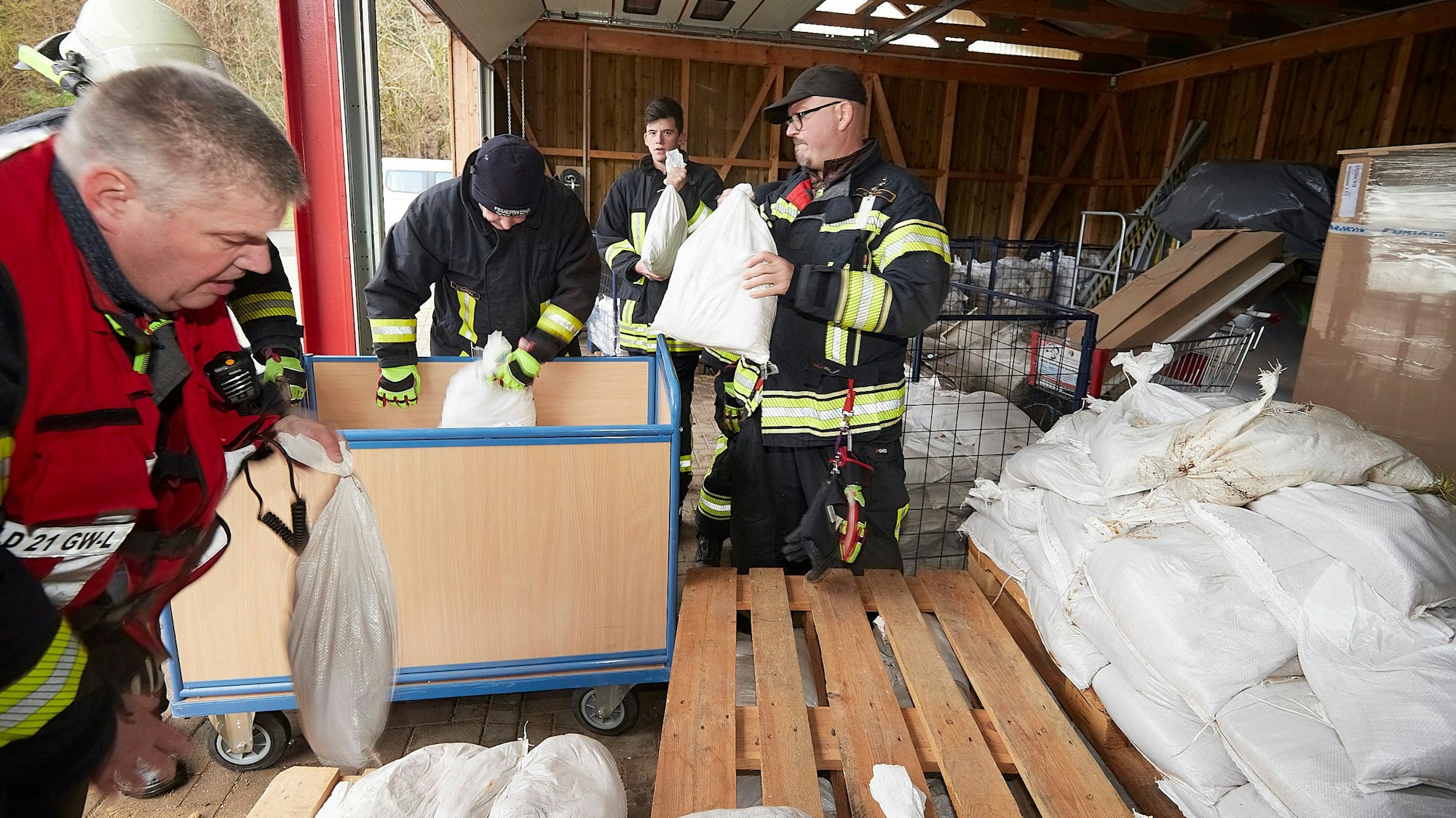 Mehrere Feuerwehrleute aus Gemünd stehen in einer Lagerhalle. Dort holen sie Sandsäcke ab.