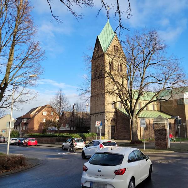 Zu sehen ist eine Kreuzung, mehrere nach links abbiegende Autos, eine Radfahrerin und im Hintergrund eine Kirche.