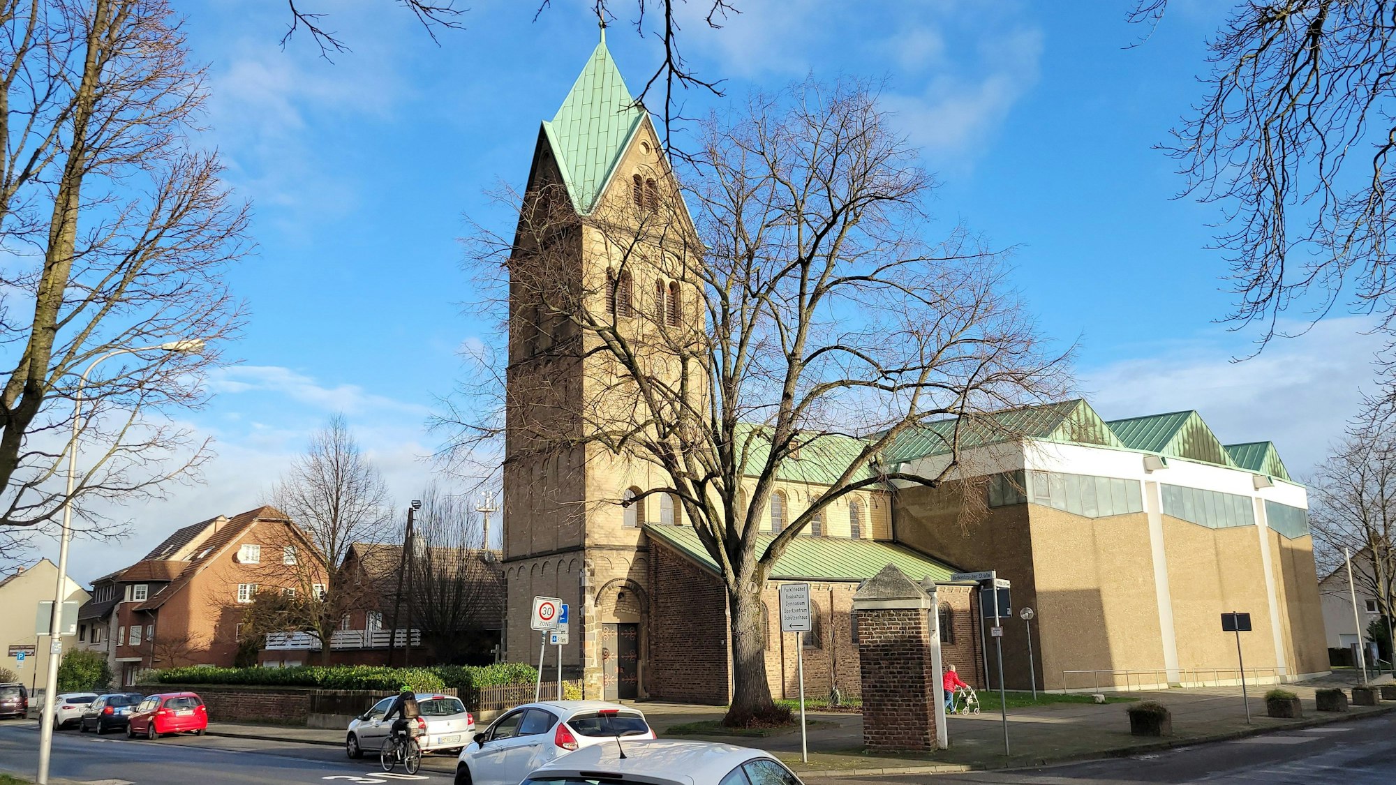 Auf einer Kreuzung biegen zwei Fahrzeuge nach links ab, im Hintergrund ist eine Kirche zu sehen.