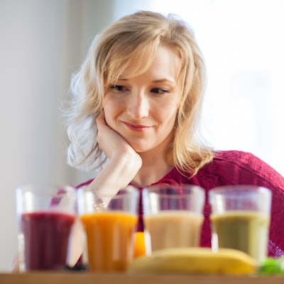 Eine blonde Frau blickt auf vier Säfte unterschiedlicher Farbe.