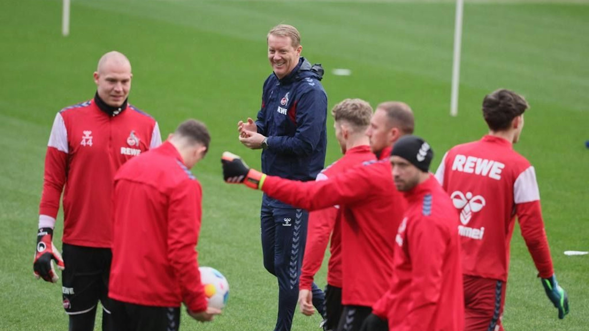 Timo Schultz steht mit Spielern des 1. FC Köln auf einem Rasen.