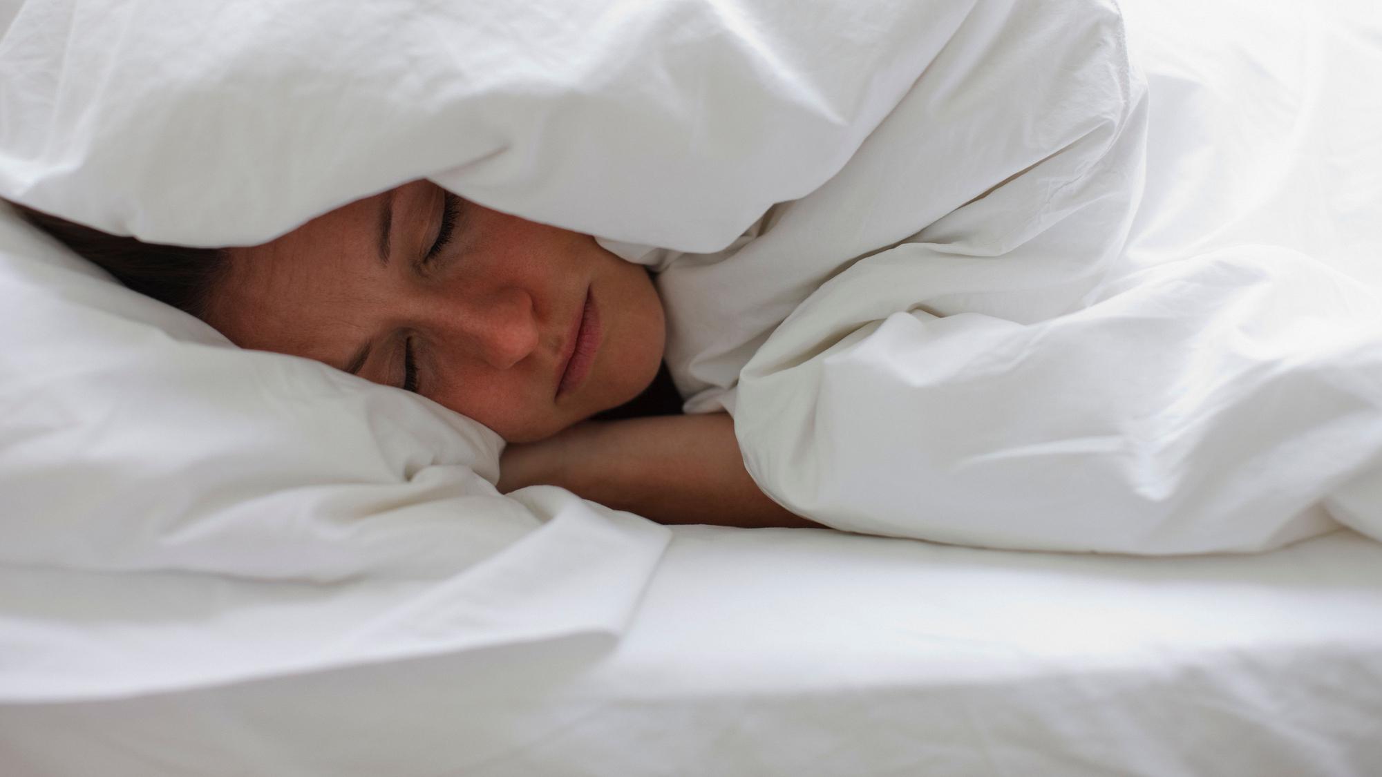 Kranke Frau liegt im Bett und zieht sich die Decke über den Kopf