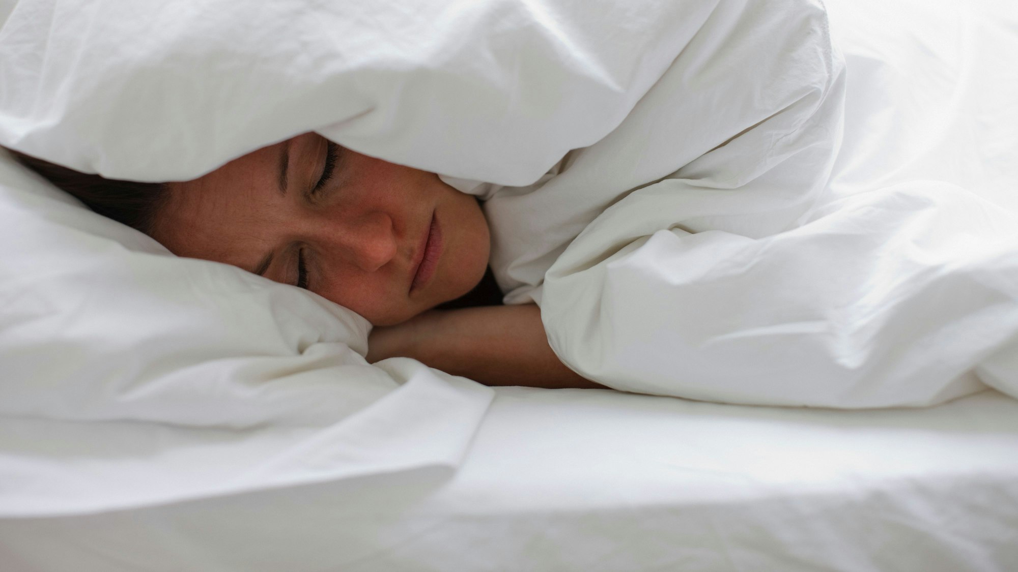 Kranke Frau liegt im Bett und zieht sich die Decke über den Kopf