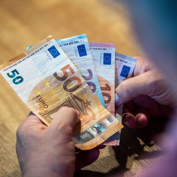 Ein älterer Mann sitzt an einem Tisch und einen 50-Euro-Schein, einen 20- und zwei 10-Euro-Scheine in der Hand.