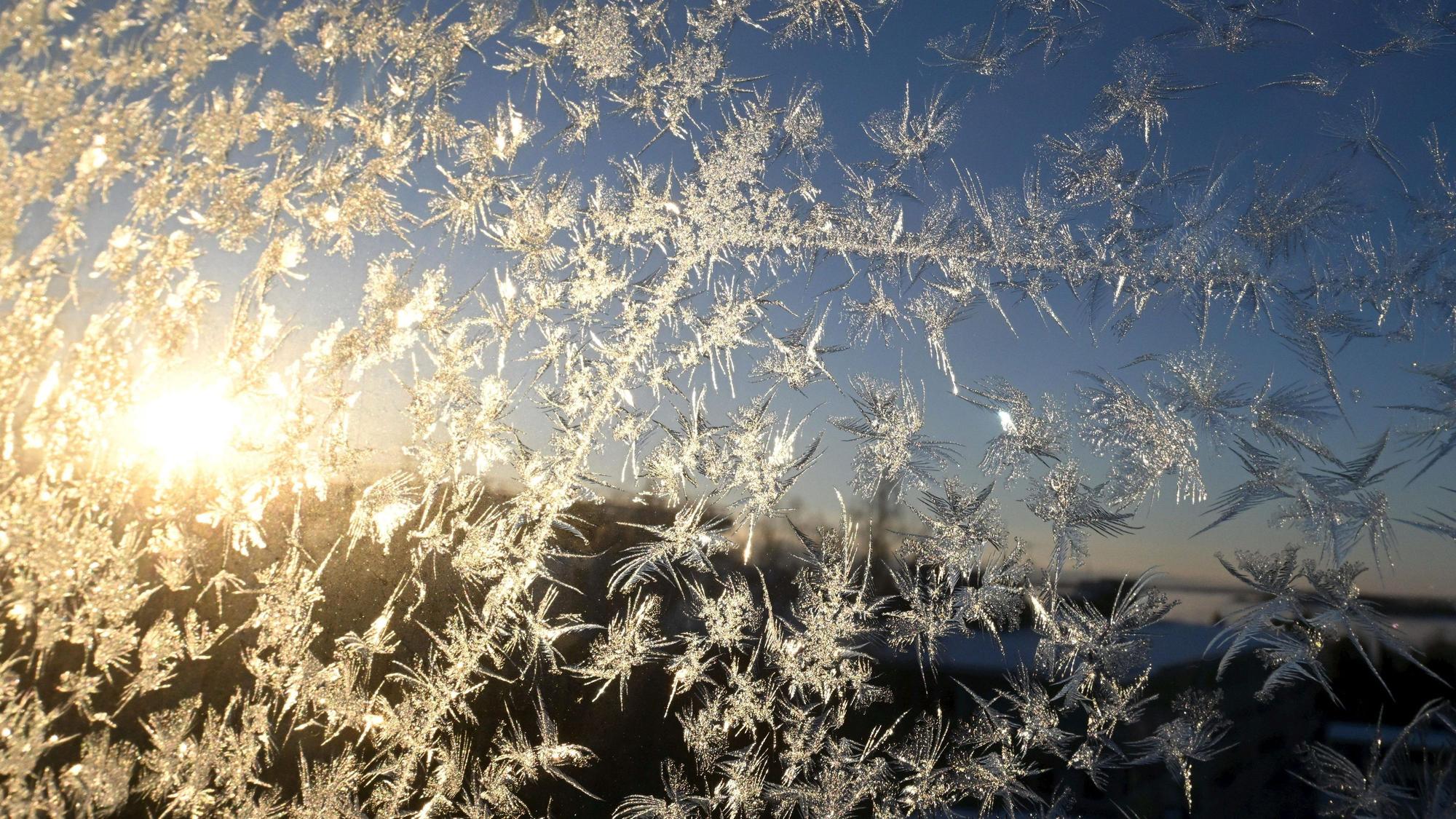 Sonnenlicht fällt auf Eiskristalle, die sich an einer Fensterscheibe gebildet haben.