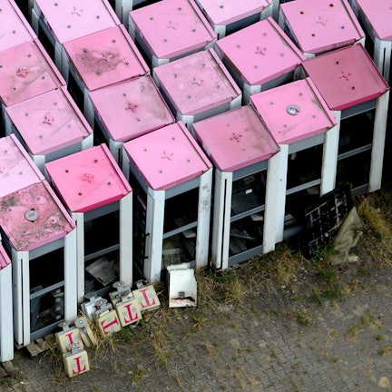 Die Luftbildaufnahme zeigt ausrangierte Telefonzellen der Telekom mit magenatfarbenen Dächern.