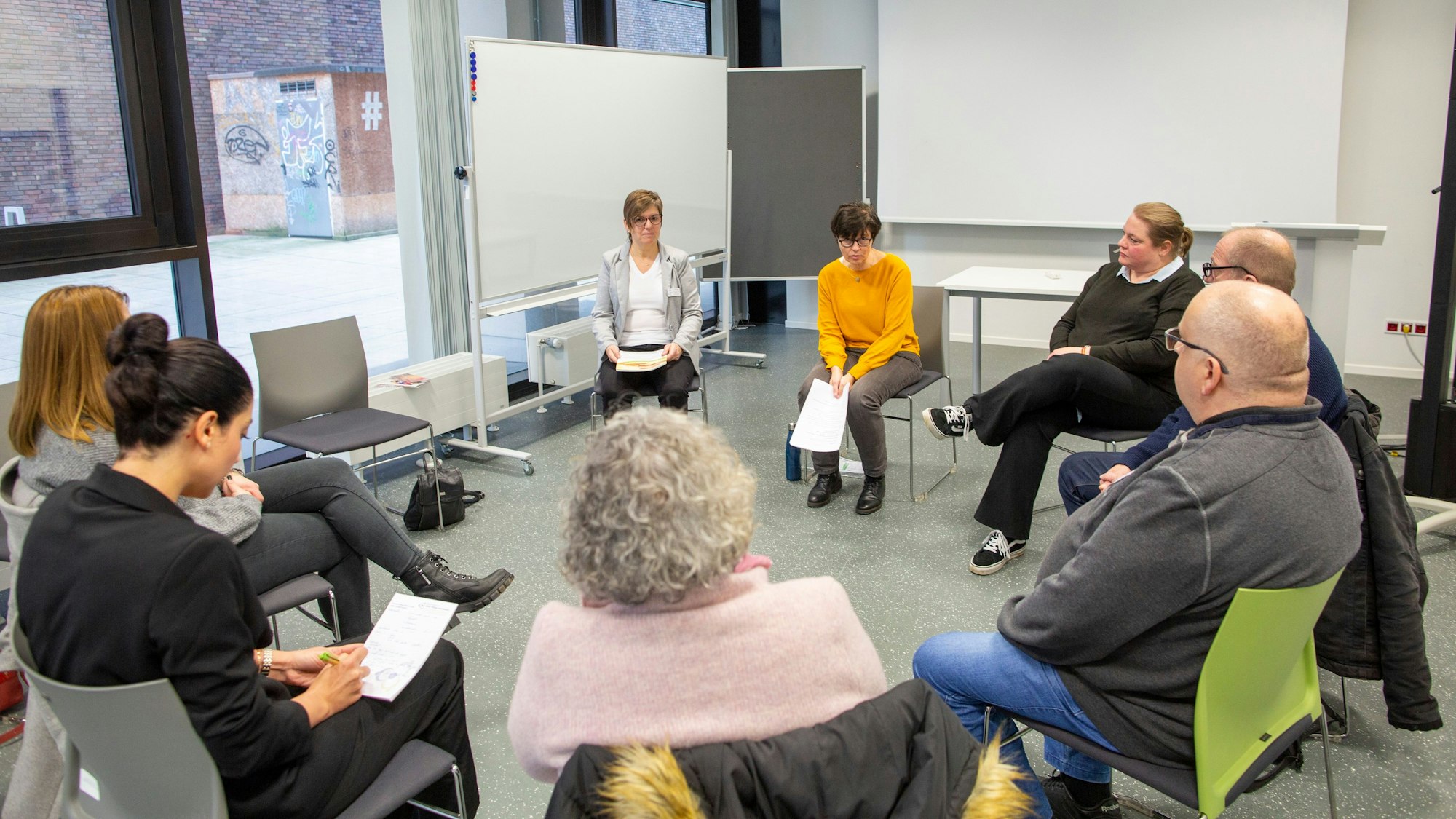 Frauen und Männer sitzen im Kursraum und hören einer Referentin zu.