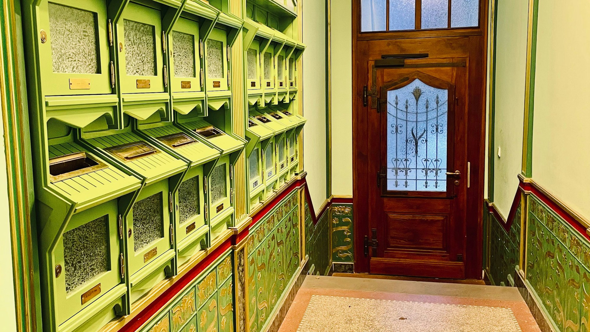 Ein Hausflur mit Briefkäste und verzierten Fliesen und Steinboden erinnert ans ausgehende 19. Jahrhundert.